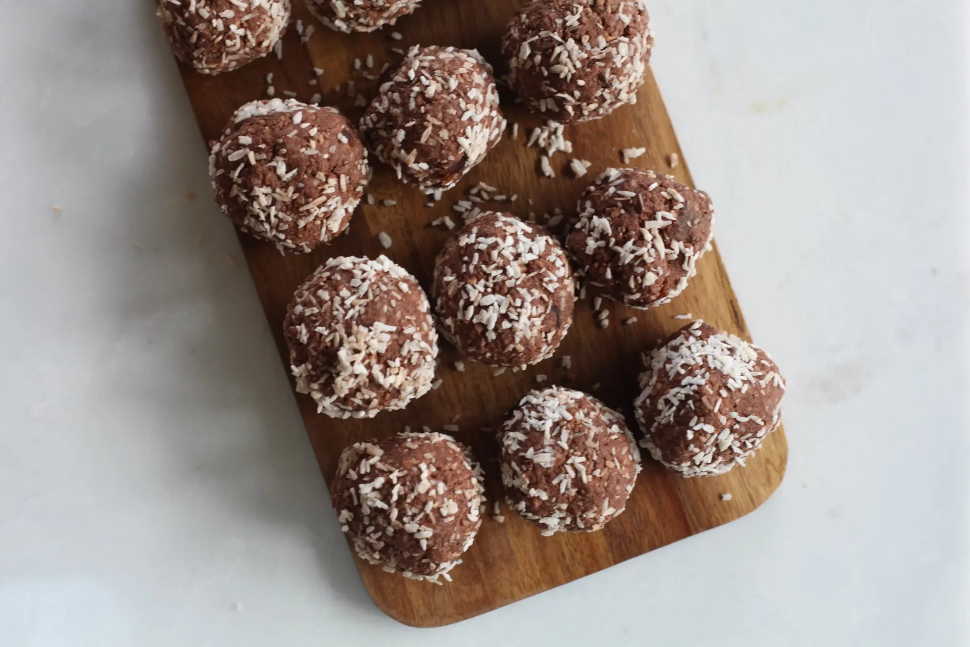 Chocolate bliss balls rolled in shredded coconut on a wooden serving board