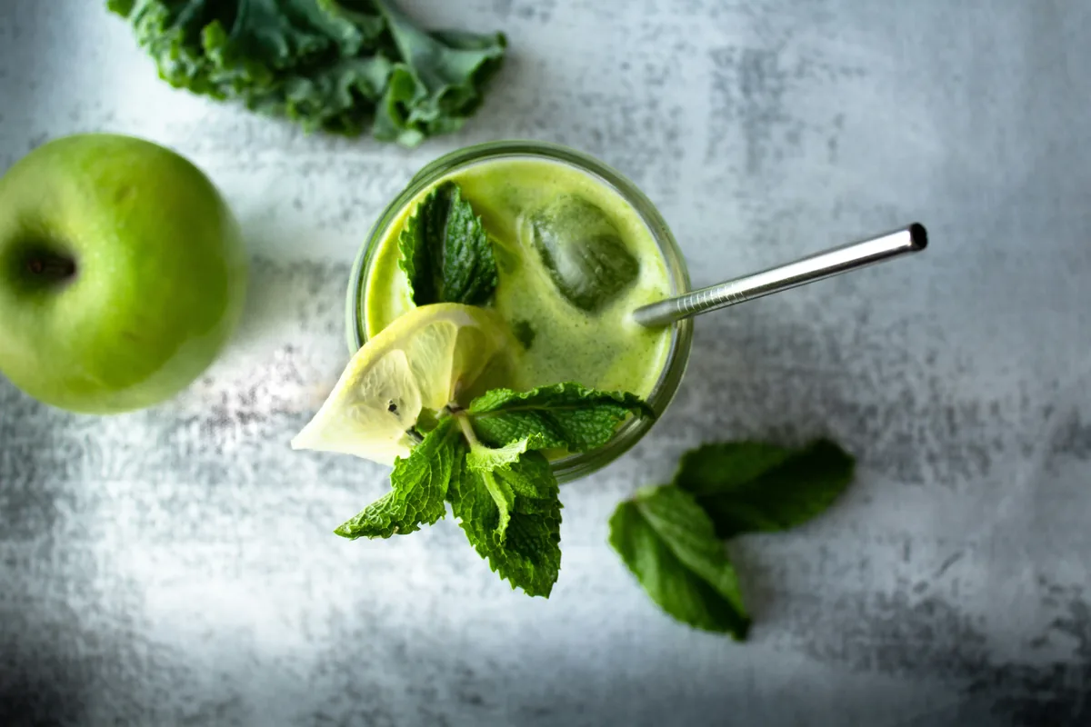 Green smoothie with lemon and mint beside a green apple and kale
