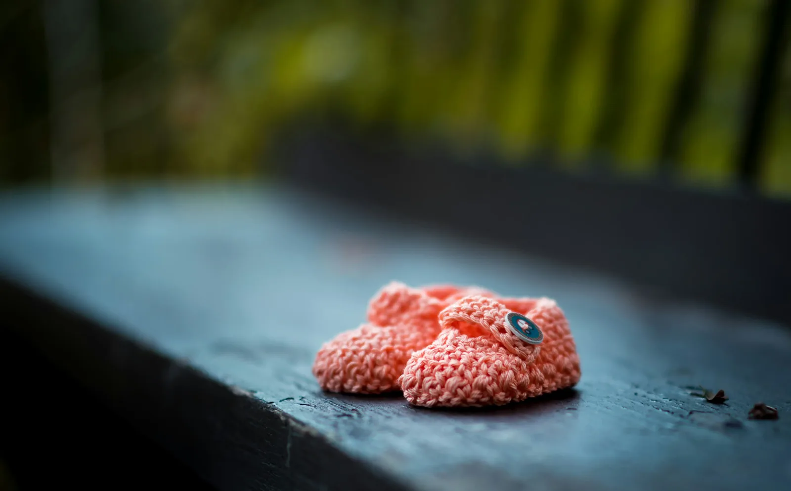 Pair of pink knitted baby booties on a dark surface