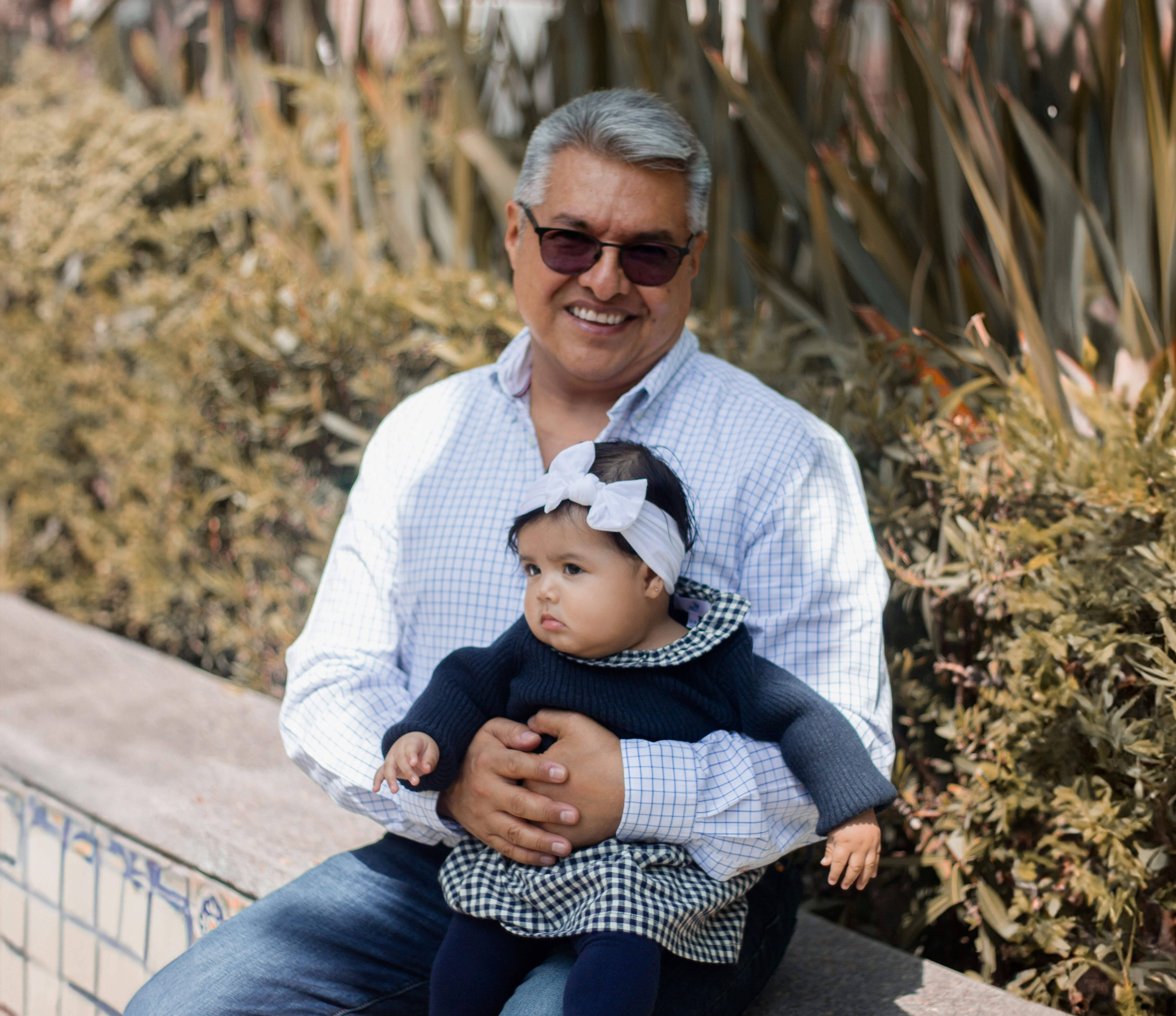 Raúl hoy, sonriendo con sus lentes de sol mientras carga a su nieta en brazos