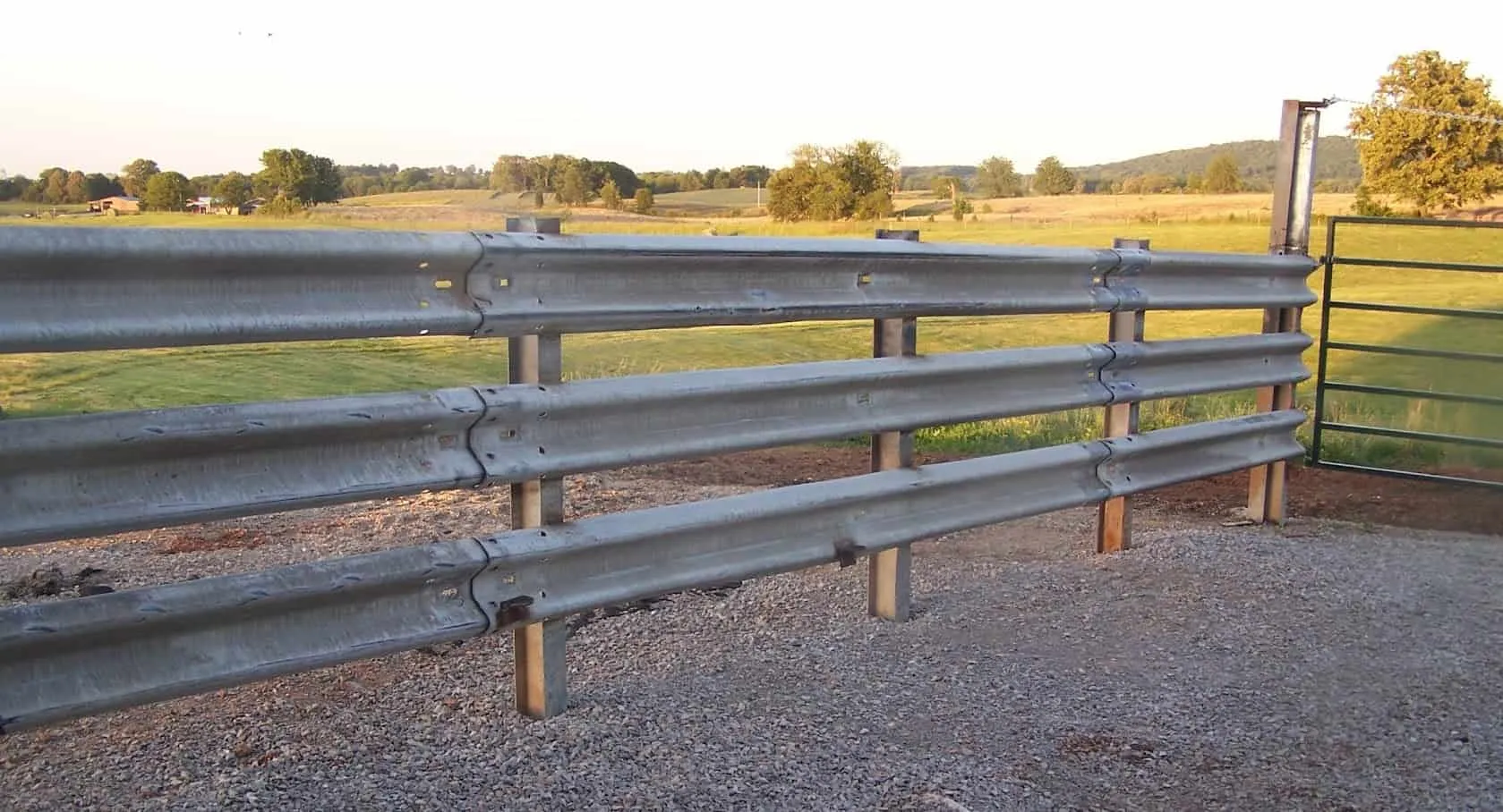 Three-rail guardrail fence along a gravel pad