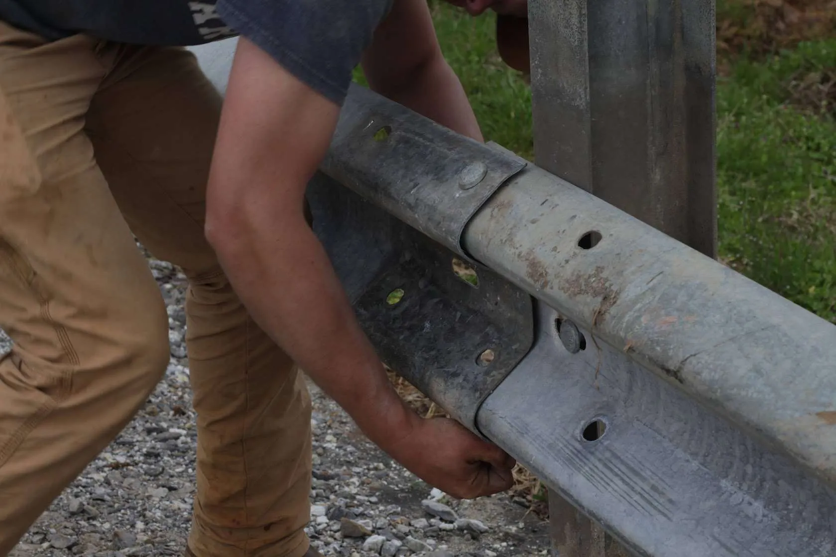 Worker bolting a used guardrail panel to a post
