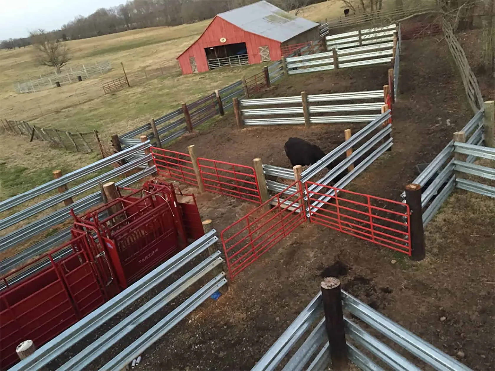 Guardrail corral pens with red gates beside a barn