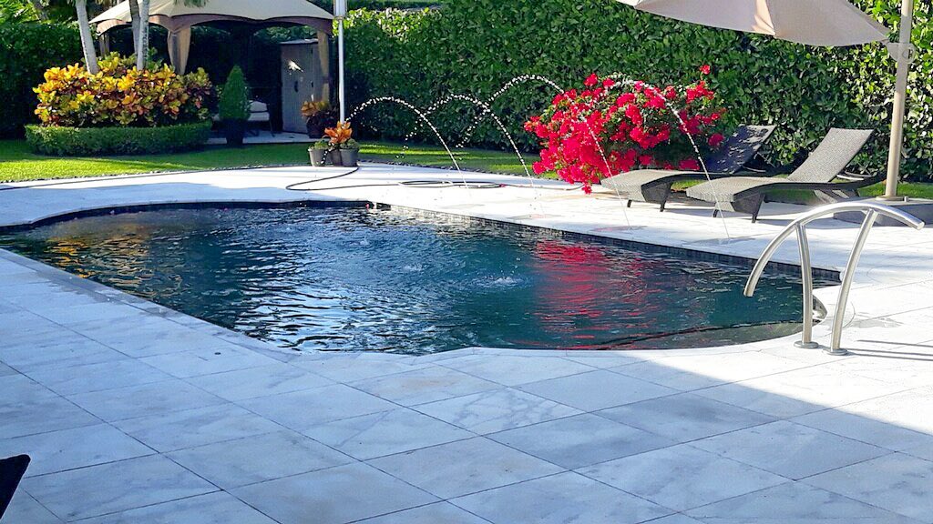Pool with custom deck jets and water features tropical landscaping and red flowers Miami - water feature design by Gables Pool