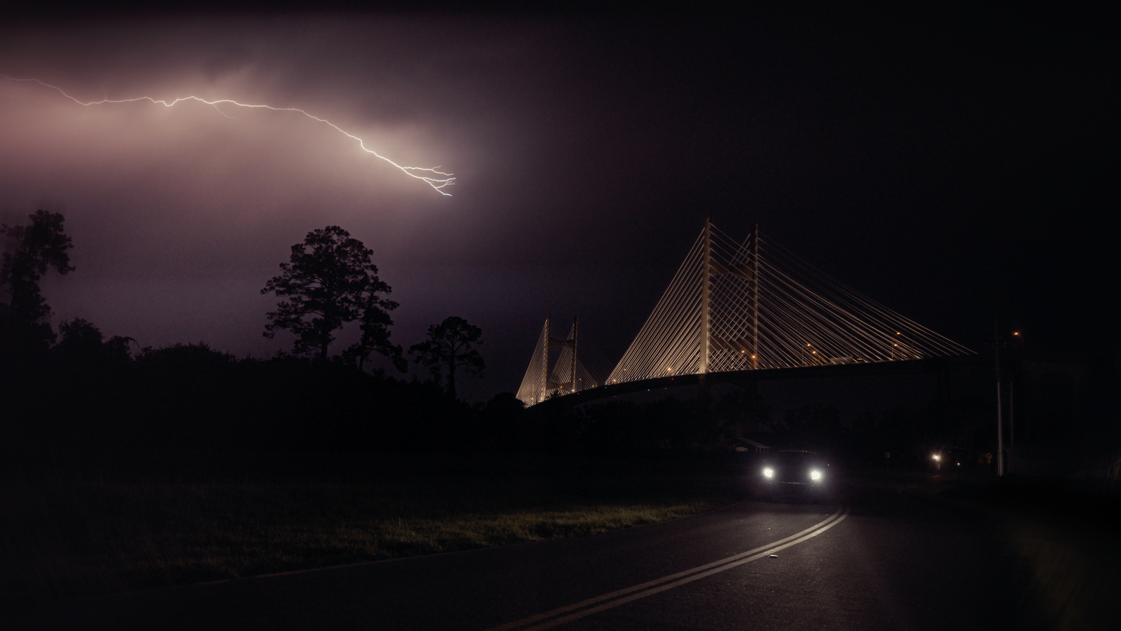 Lightning strikes over a cable-stayed bridge at night as a car approaches, from the documentary The Calm and The Storm