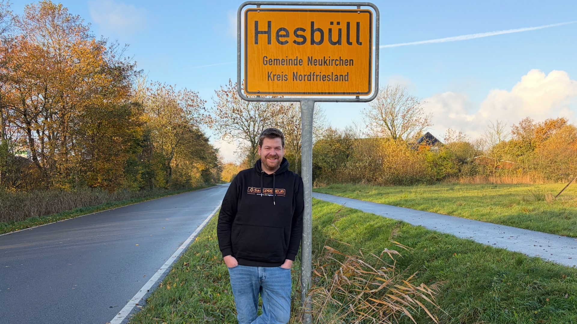 Martin Dellwing lehnt am Ortseingangs-Schild von Hesbüll