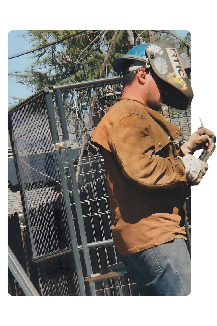 Professional welder in leather jacket and welding helmet fabricating a custom metal gate outdoors