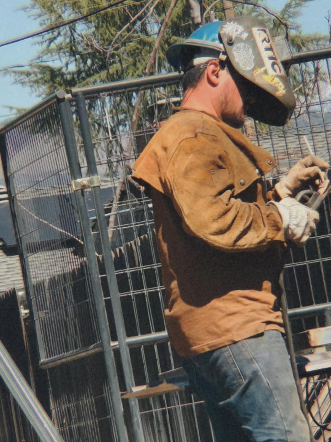 Professional welder in leather jacket and welding helmet fabricating a custom metal gate outdoors