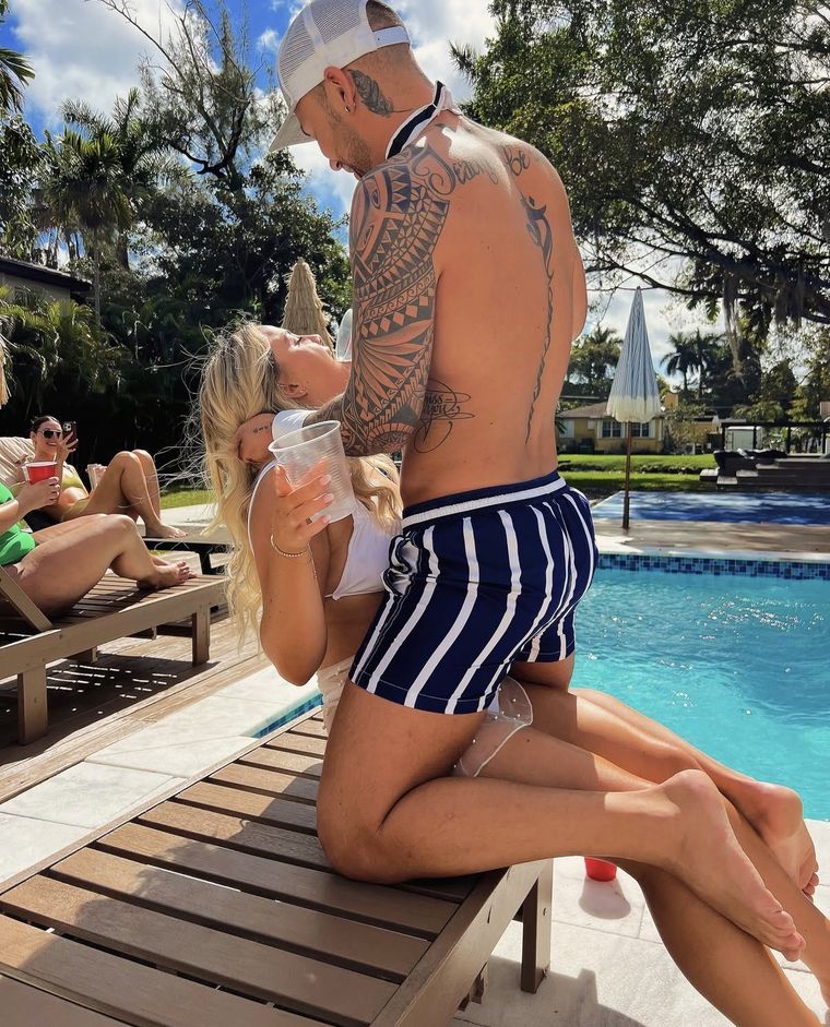 A Cheeky Butler in swim shorts dancing with a guest on a poolside lounger