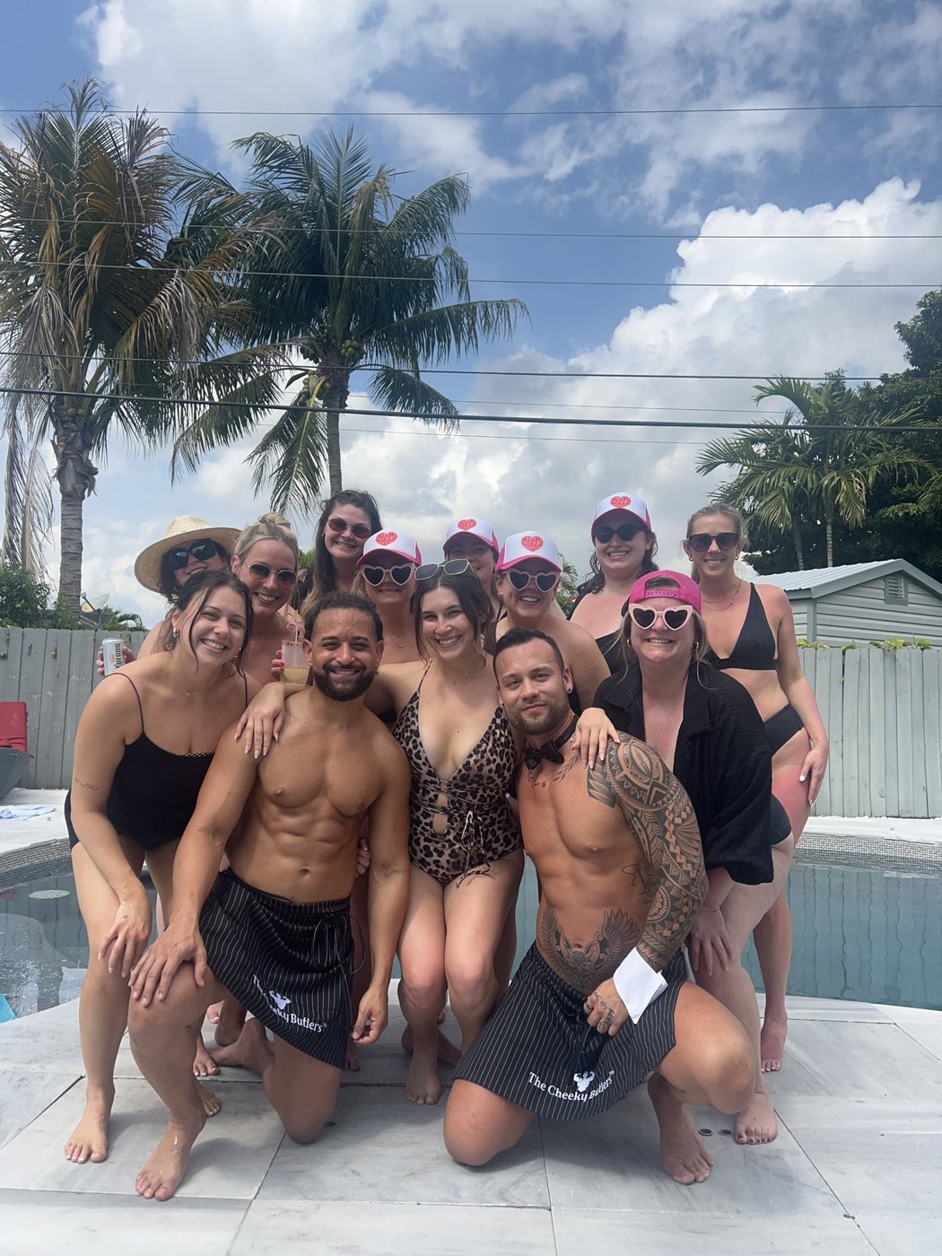 A bachelorette group in pink party hats around the pool with two Cheeky Butlers