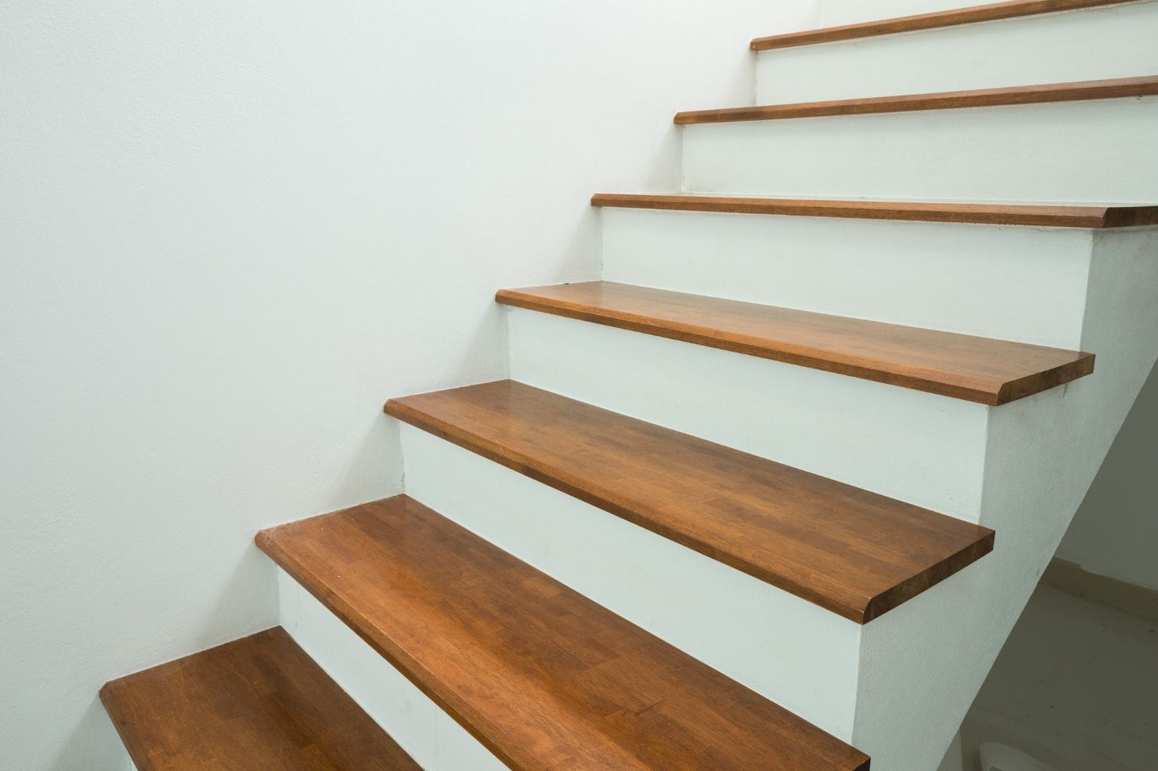 Escalier intérieur rénové avec un habillage de marches en bois sombre sur une structure blanche épurée.