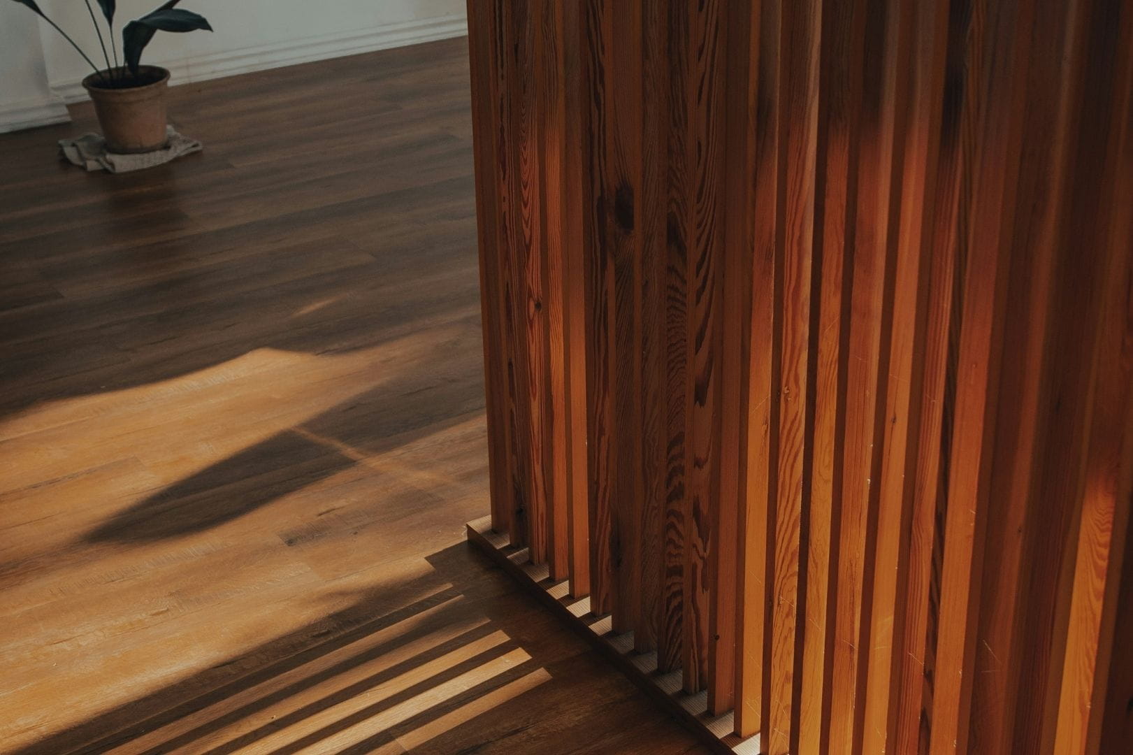 Brise-vue décoratif type claustra en bois à lames verticales installé à l'intérieur d'une maison en rénovation.