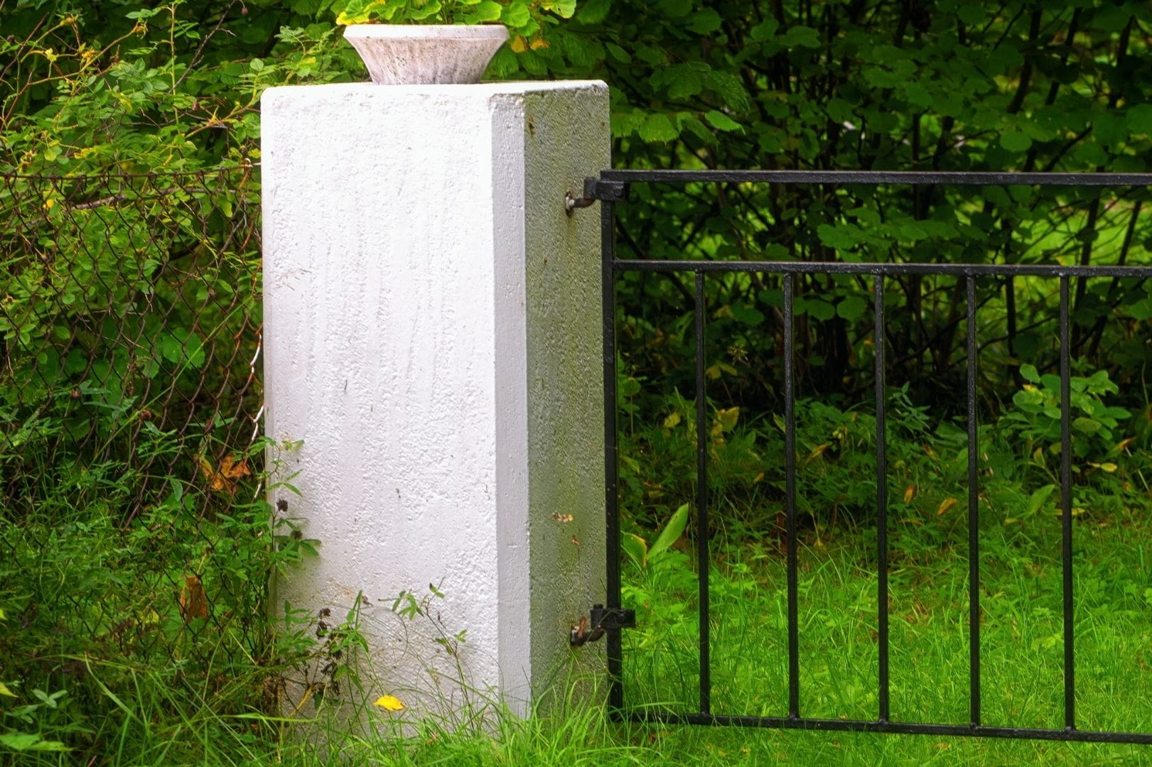 Construction d'un pilier de clôture maçonné blanc avec fixation de portail métallique en bordure de jardin.