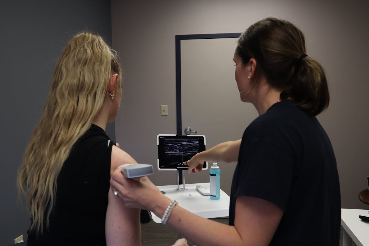 A healthcare professional performs an ultrasound shoulder scan, pointing at the screen for analysis. A healthcare professional performs an ultrasound shoulder scan, pointing at the screen for analysis.