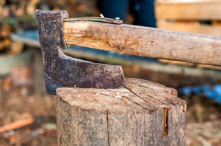 A close-up of a weathered, metal-headed axe resting firmly in a wooden chopping block, representing professional wood preparation and maintenance services by SGJ Landscaping in Honesdale, PA.