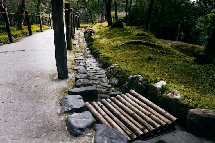 A peaceful garden path featuring a natural stone border and a traditional bamboo drainage grate, set against lush green moss, by SGJ Landscaping in Honesdale, PA.