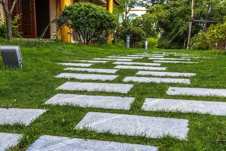 A modern stone stepping-stone pathway set into a vibrant green lawn, leading toward a garden landscape, professionally installed by SGJ Landscaping in Honesdale, PA.