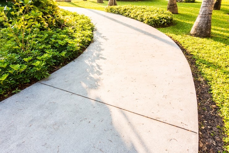 A smooth, professionally installed concrete pathway winding through a beautifully landscaped garden with manicured shrubs and trees, by SGJ Landscaping in Honesdale, PA.