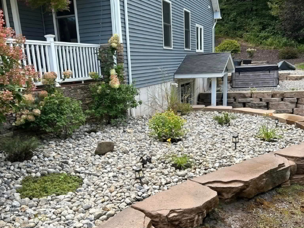 Low maintenance rock landscape with stone edging and drought tolerant plants near a home.