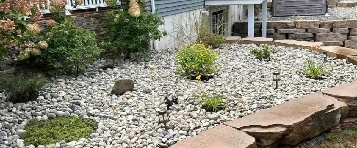 A landscaped rock garden featuring various plants, small shrubs, and solar lights, bordered by terraced stone walls.