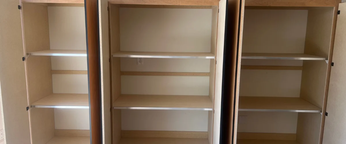 Three empty wooden cabinet units with light-colored shelving inside, including a power outlet in the middle unit.