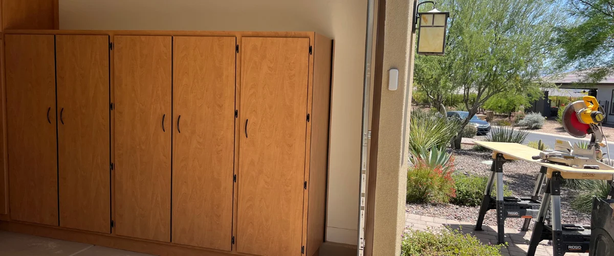 A garage interior with light brown wooden cabinets opens to a sunlit outdoor area with a miter saw set up on Saw RIDGE saws. A garage interior with light brown wooden cabinets opens to a sunlit outdoor area with a miter saw set up on Saw RIDGE saws.