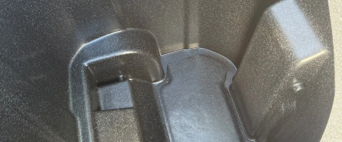 Close-up detail of a dark, textured, molded plastic part with shiny highlights and various angles.