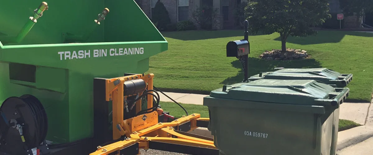 A bright green trash bin cleaning trailer on a street with two green trash bins next to a mailbox. A bright green trash bin cleaning trailer on a street with two green trash bins next to a mailbox.