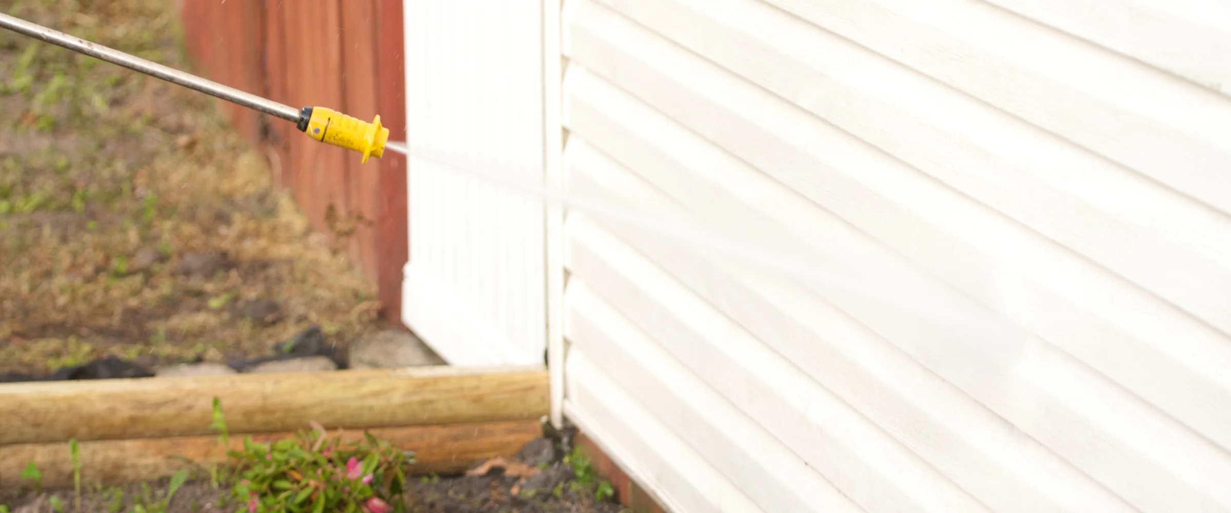 A power washer spraying a strong stream of water onto white residential siding, cleaning the exterior.