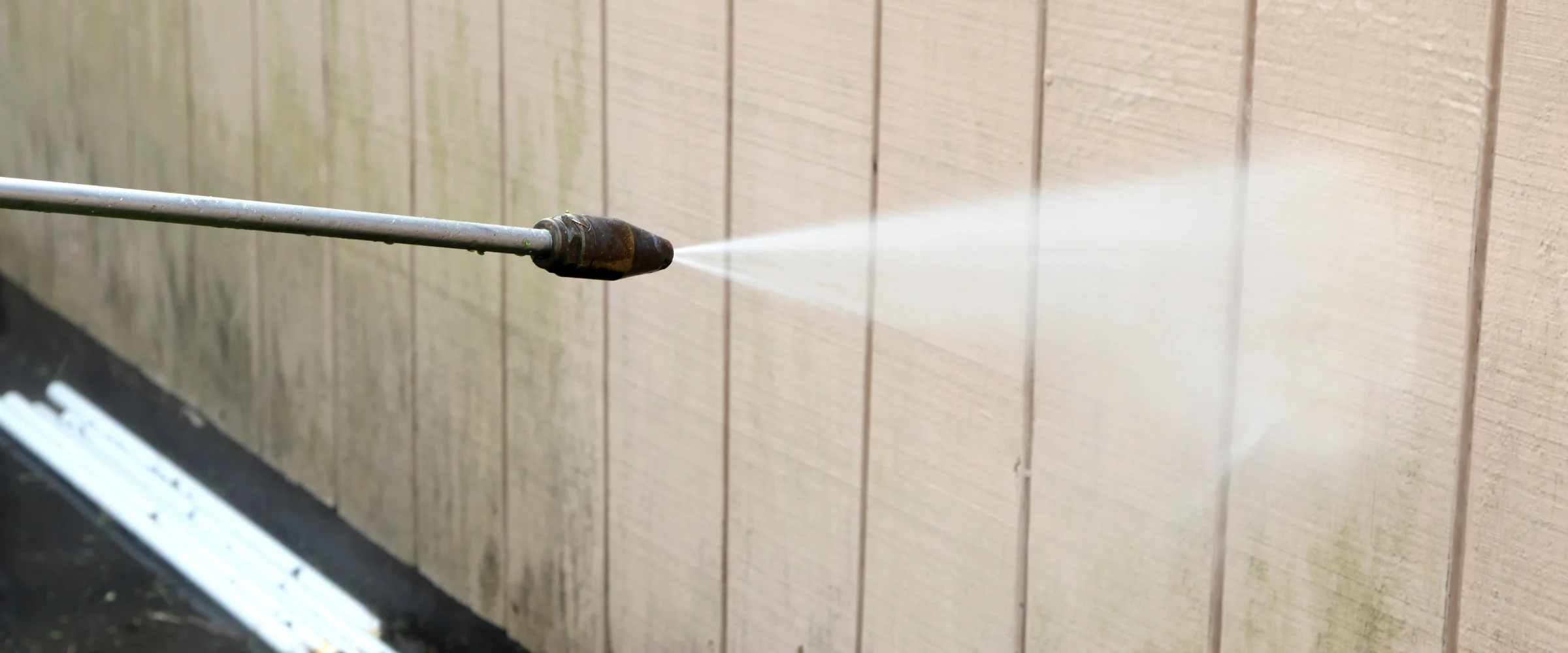 A person uses a pressure washer to clean dirty white house siding, removing grime with a powerful spray. A person uses a pressure washer to clean dirty white house siding, removing grime with a powerful spray.