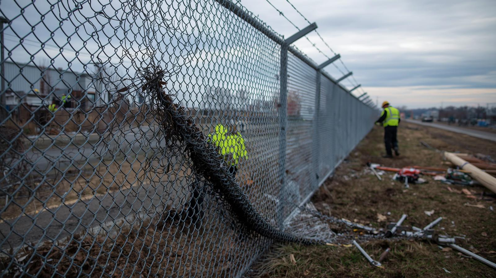 Storm-damaged commercial fence with fallen panels and leaning posts requiring repair. Storm-damaged commercial fence with fallen panels and leaning posts requiring repair.