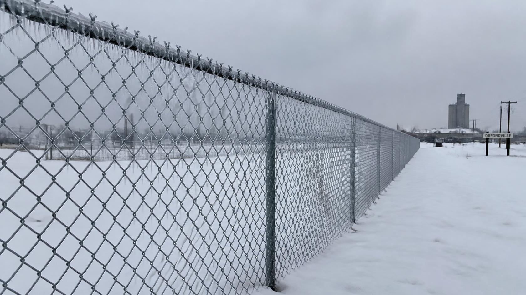 Commercial chain link fence in Orfordville, WI being prepared for snow and ice with attention to posts, mesh, gates, and perimeter security.
