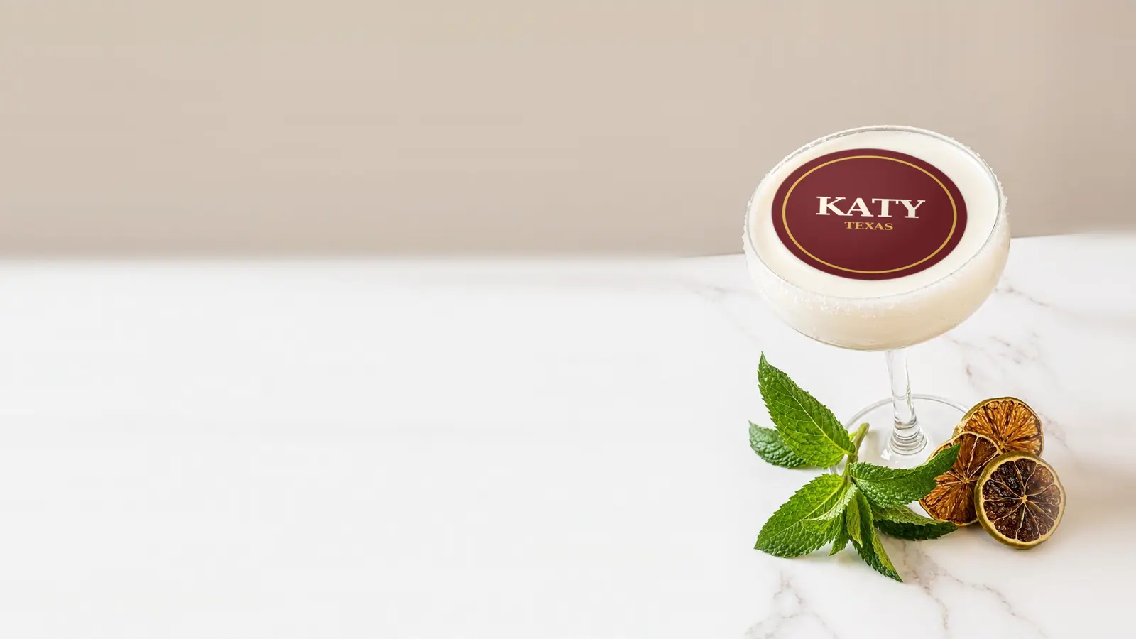 Coupe cocktail topped with a round edible frosting sheet topper printed with the name Katy, Texas, in a gold ring