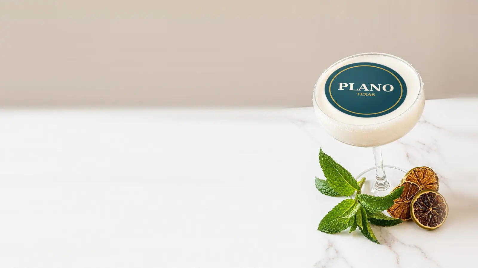 Coupe cocktail topped with a round edible frosting sheet topper printed with the name Plano, Texas, in a gold ring