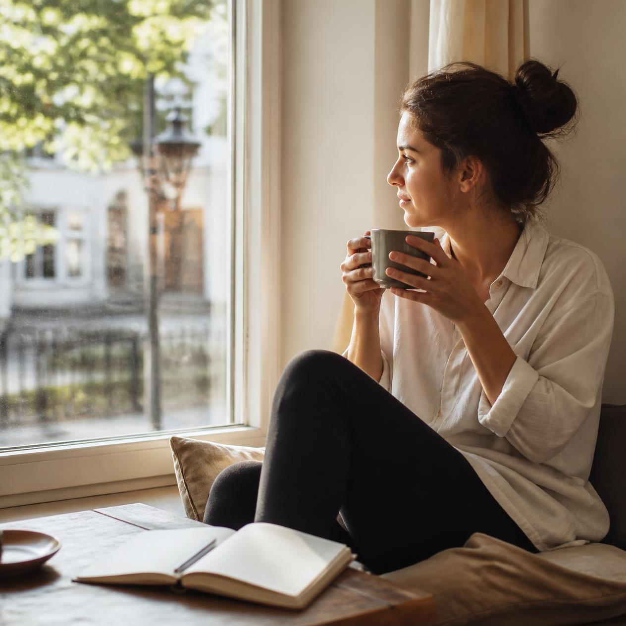 A relaxed person sitting by a window with a cup of coffee, looking out calmly, soft morning light, open notebook nearby, photorealistic, peaceful and unhurried mood A relaxed person sitting by a window with a cup of coffee, looking out calmly, soft morning light, open notebook nearby, photorealistic, peaceful and unhurried mood