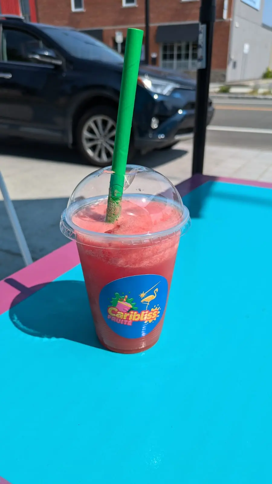 Smoothie rouge avec paille verte sur table turquoise devant la boutique Caribliss