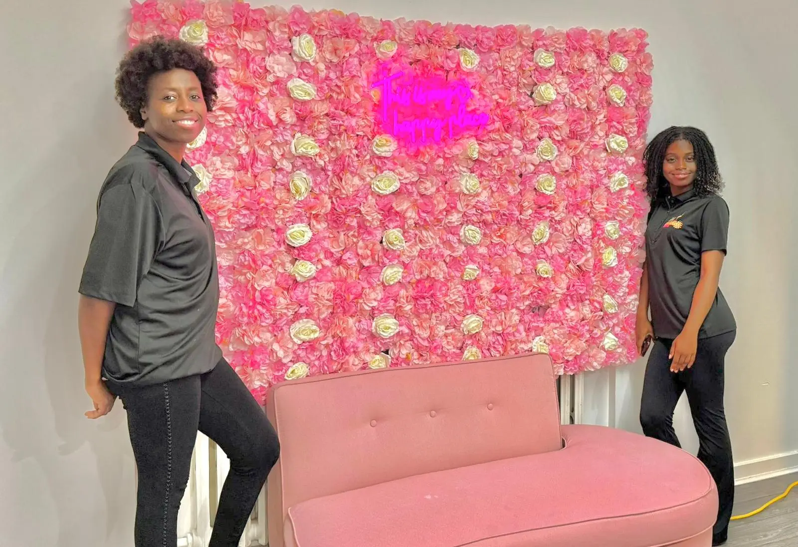 Les deux fondatrices de Caribliss Fruité, mère et fille, devant le mur de fleurs roses du comptoir