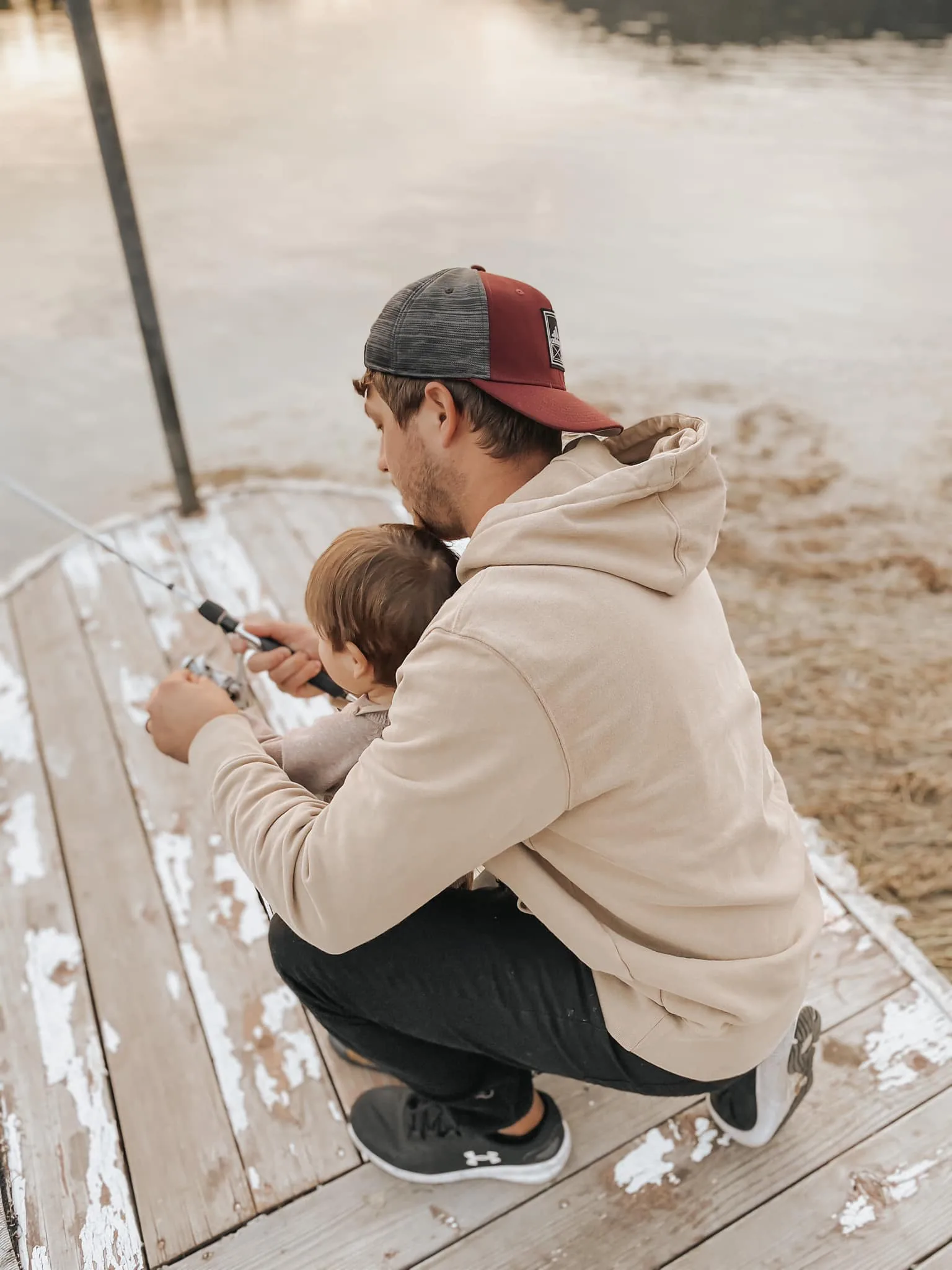 Tanner kneeling on a wooden lake dock teaching his young son how to fish