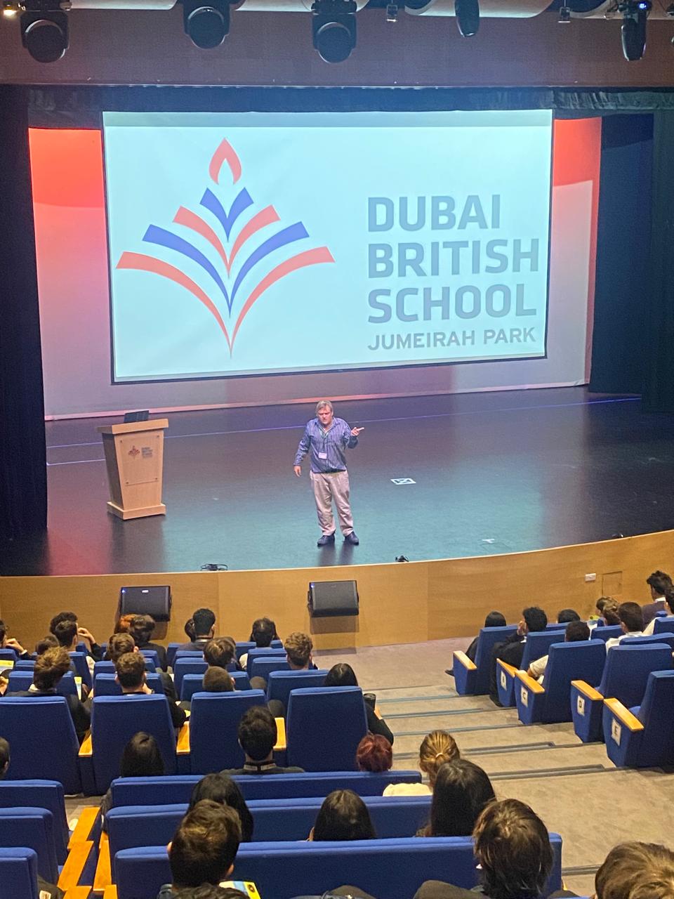 Paul Tosio on stage presenting to a full auditorium at Dubai British School, Jumeirah Park
