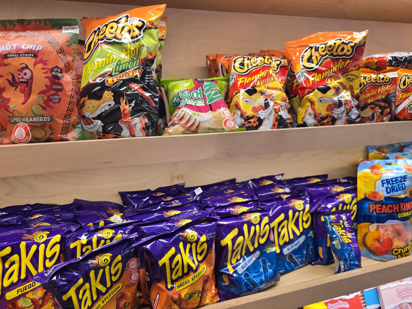 Display of familiar American snack brands including Cheetos and Takis in an overseas convenience store. Display of familiar American snack brands including Cheetos and Takis in an overseas convenience store.