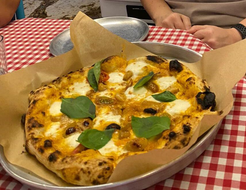 Fresh wood-fired pizza served on a metal tray at a restaurant table with a red checkered tablecloth. Fresh wood-fired pizza served on a metal tray at a restaurant table with a red checkered tablecloth.