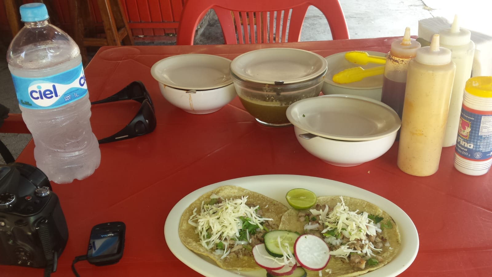 Plate of street-style tacos with cheese, radishes, cucumber, and lime served on a red table at a casual taco stand in Mexico. Plate of street-style tacos with cheese, radishes, cucumber, and lime served on a red table at a casual taco stand in Mexico.