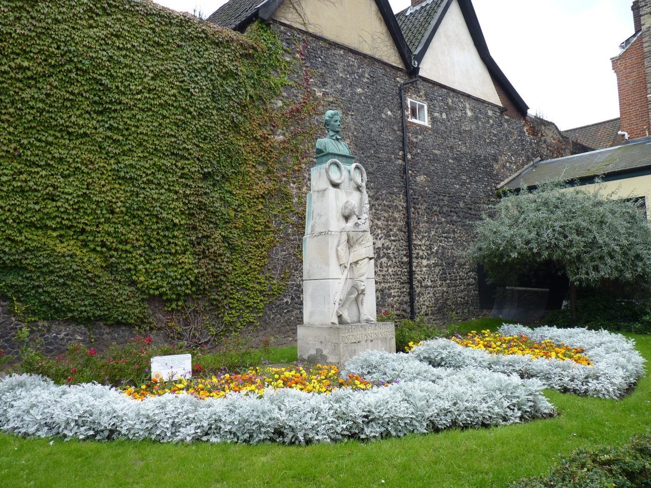 Memorial statue of Edith Cavell in a landscaped garden with flowers and ivy-covered wall, honoring the nurse executed during World War I in Norwich. Memorial statue of Edith Cavell in a landscaped garden with flowers and ivy-covered wall, honoring the nurse executed during World War I in Norwich.
