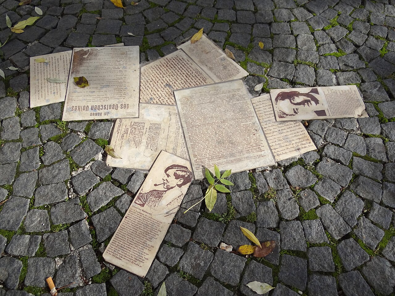 Memorial display of scattered documents and portraits commemorating the White Rose movement on cobblestone pavement, honoring student resistance to the Nazi regime in Munich. Memorial display of scattered documents and portraits commemorating the White Rose movement on cobblestone pavement, honoring student resistance to the Nazi regime in Munich.