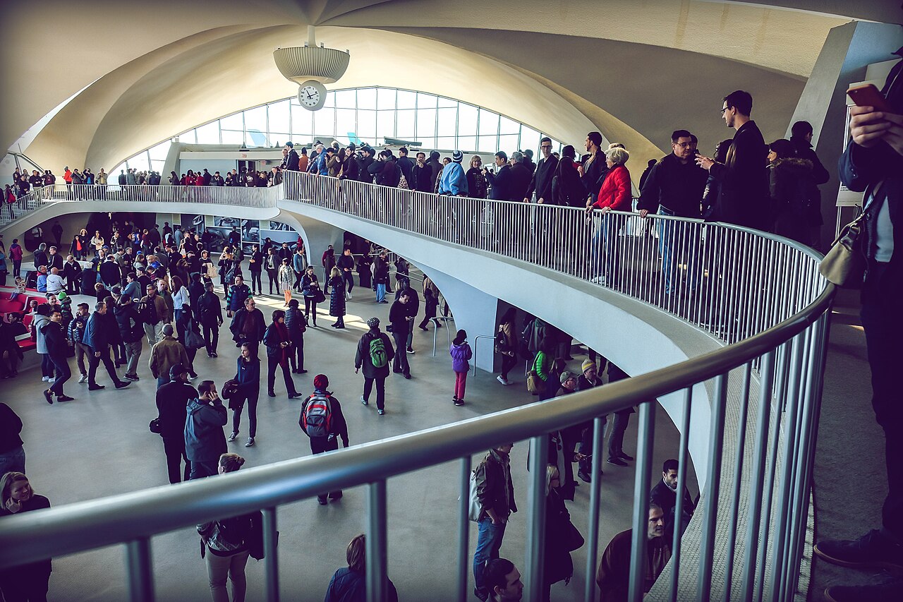 Crowded TWA Flight Center with travelers across multiple levels, illustrating congestion and system strain in modern air travel.