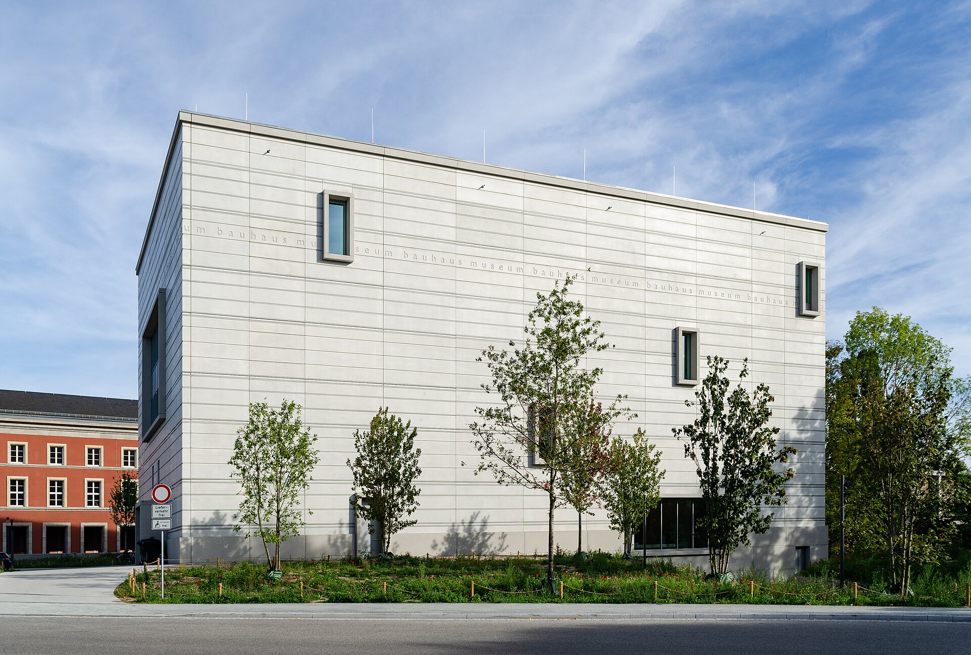 Exterior view of the Bauhaus Museum in Weimar, Germany, featuring minimalist modernist architecture, clean geometric lines, narrow windows, and landscaped greenery beneath a blue sky.