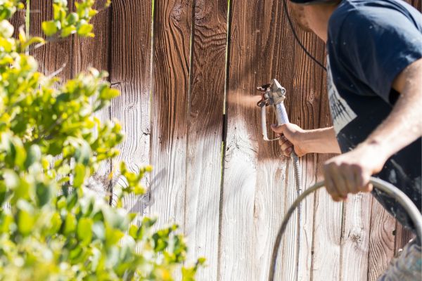 Worker applying stain to a weathered wooden fence using a spray gun for restoration..jpg Worker applying stain to a weathered wooden fence using a spray gun for restoration..jpg