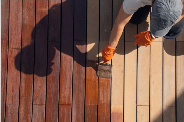 man wearing a cap and gloves staining a deck
