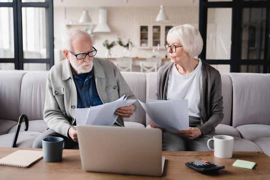 An older couple on the sofa with a laptop and letters