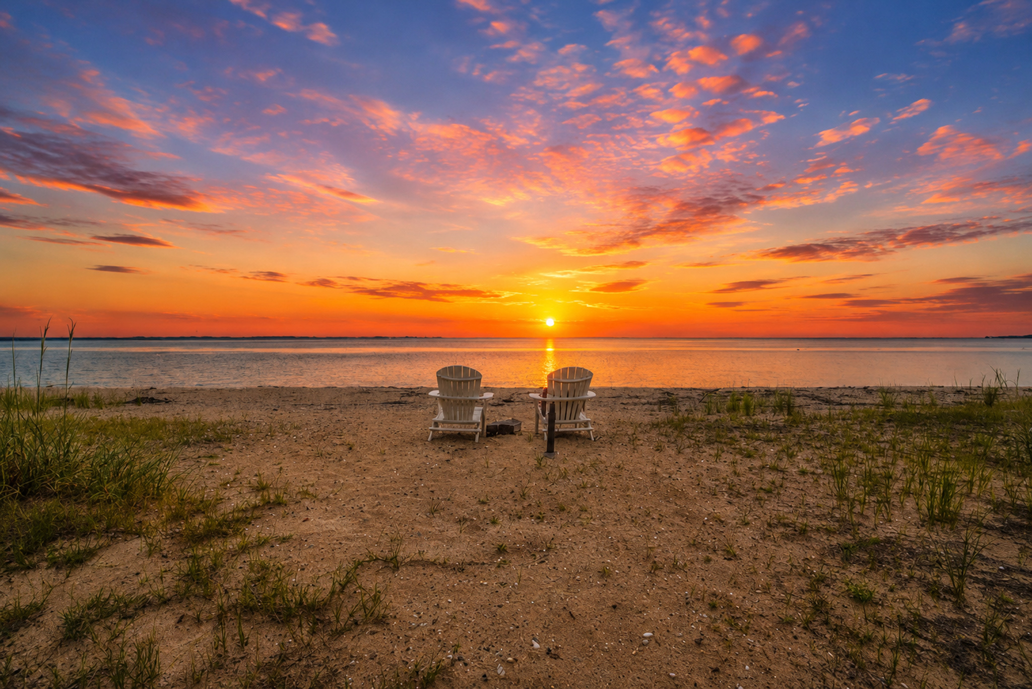 Sunset over the Chesapeake Bay in Southern Maryland with two Adirondack chairs on the shoreline